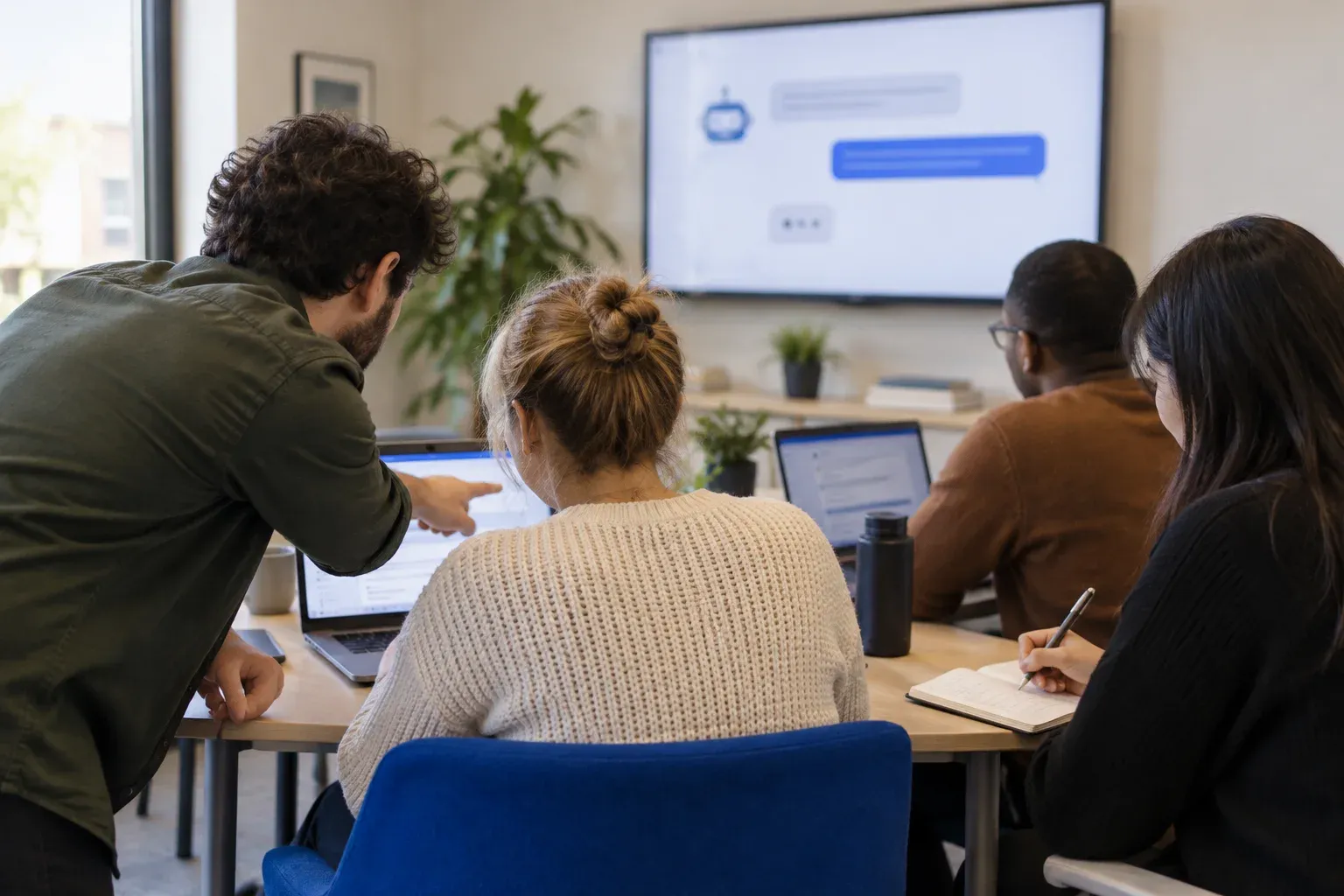A hands-on training session: one person leans in to point at a colleague's laptop while others take notes
